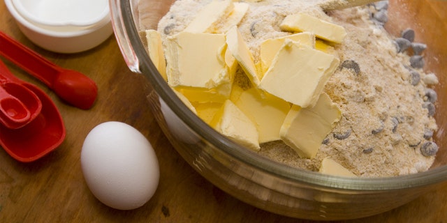 Photo of chocolate chip cookie dough being mixed. Focus is on the butter and egg.