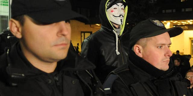 Police officers block the entrance to the National Electoral Office as a man wearing a mask stands behind, in Warsaw, Poland, Thursday, Nov. 20, 2014. Earlier a group of right wing activists entered the building and began to occupy it demanding the members of the National Electoral Office to resign. Prosecutors are investigating a hacking attack on the website of Poland's voting commission, while a top official has resigned over irregularities that are delaying the vote count in recent local elections. (AP Photo/Alik Keplicz)
