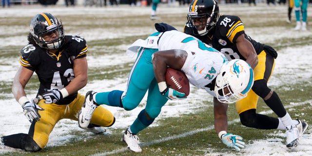 Miami Dolphins tight end Charles Clay (42) slips the tackle of Pittsburgh Steelers strong safety Troy Polamalu (43) and Pittsburgh Steelers cornerback Cortez Allen (28) and heads to the end zone for a touchdown during the second half of an NFL football game in Pittsburgh, Sunday, Dec. 8, 2013. (AP Photo/Don Wright)