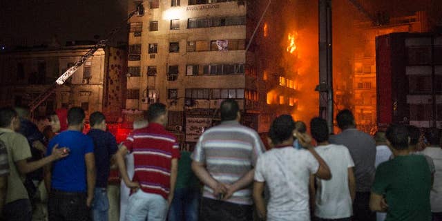 People look at a fire that erupted inside a six-story hotel called Andalusia in the populous Ataba neighborhood in Cairo, Egypt, Monday, May 9, 2016. A massive fire erupted early hours Monday morning in a busy low-price commercial area in downtown Cairo, injuring at least 60 mostly from suffocation. There were no reports of deaths. (AP Photo/Sabry Khaled)