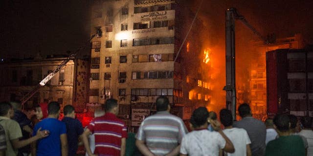 People look at a fire that erupted inside a six-story hotel called Andalusia in the populous Ataba neighborhood in Cairo, Egypt, Monday, May 9, 2016. A massive fire erupted early hours Monday morning in a busy low-price commercial area in downtown Cairo, injuring at least 60 mostly from suffocation. There were no reports of deaths. (AP Photo/Sabry Khaled)