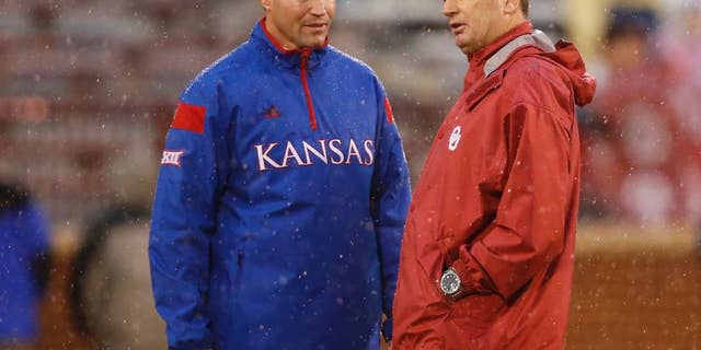 Kansas head coach Clint Bowen, left, and Oklahoma head coach Bob Stoops, right, talk before the start of their weather delayed NCAA college football game in Norman, Okla., Saturday, Nov. 22, 2014. The start time was pushed back at least 90 minutes due to lightning. (AP Photo/Sue Ogrocki)