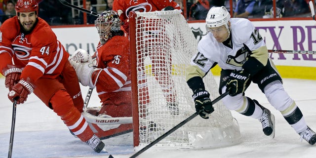Pittsburgh Penguins' Chuck Kobasew (12) and Carolina Hurricanes' Jay Harrison (44) reach for the puck as Hurricanes goalie Justin Peters (35) defends the goal during the first period of an NHL hockey game in Raleigh, N.C., Monday, Oct. 28, 2013. (AP Photo/Gerry Broome)
