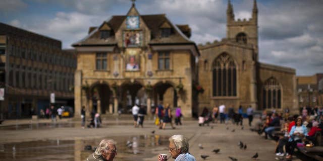In this Wednesday, July 6, 2016 photo, a couple drink coffee in front of the Guildhall, also known as the Butter Cross, on Cathedral Square, in downtown Peterborough, East of England. Many people who voted for Britain to get out of the European Union look at multi-ethnic Peterborough as a warning example. They say British identity has been eroded in parts of the city where migrants have moved in and pubs have been replaced by shawarma shops or ethnic food stores. (AP Photo/Emilio Morenatti)