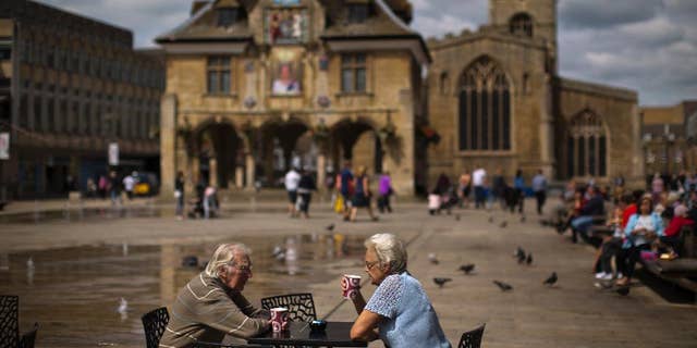 In this Wednesday, July 6, 2016 photo, a couple drink coffee in front of the Guildhall, also known as the Butter Cross, on Cathedral Square, in downtown Peterborough, East of England. Many people who voted for Britain to get out of the European Union look at multi-ethnic Peterborough as a warning example. They say British identity has been eroded in parts of the city where migrants have moved in and pubs have been replaced by shawarma shops or ethnic food stores. (AP Photo/Emilio Morenatti)