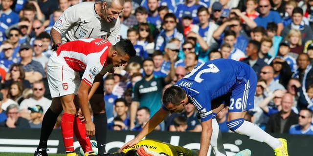 Arsenal's Alexis Sanchez, left, gets up after colliding with Chelsea's goalkeeper Thibaut Courtois, who lies on the ground attended to by teammate Chelsea's John Terry, right, during their English Premier League soccer match between Chelsea and Arsenal at Stamford Bridge stadium in London Sunday, Oct. 5, 2014. (AP Photo/Alastair Grant)