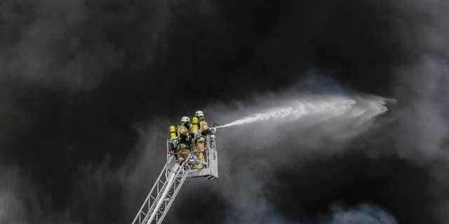 Fire fighters spray water in front of smoke at a burning storage hall of the Dong Xuan Center, an Asia market specialized in Vietnamese goods, in Berlin, Germany, Wednesday, May 11, 2016. The fire department sent some 150 trucks and other vehicles to the fire which broke out Wednesday morning . (AP Photo/Markus Schreiber)