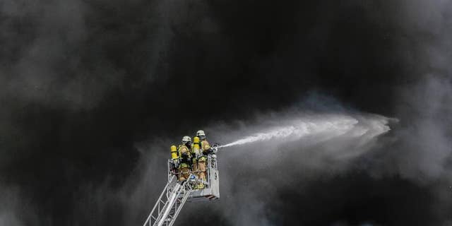 Fire fighters spray water in front of smoke at a burning storage hall of the Dong Xuan Center, an Asia market specialized in Vietnamese goods, in Berlin, Germany, Wednesday, May 11, 2016. The fire department sent some 150 trucks and other vehicles to the fire which broke out Wednesday morning . (AP Photo/Markus Schreiber)