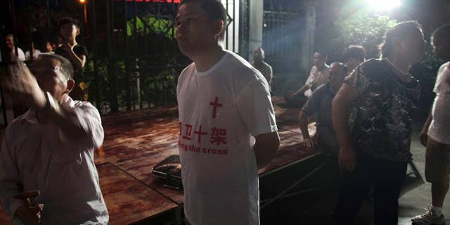 In this photo taken July 16, 2014, a church member wears a T-shirt with the Chinese words "Defend the cross" as he stakes out overnight to protect the cross from being demolished at a Christian church in Ao'jiang, Pingyang county of Wenzhou in eastern China's Zhejiang province. M(AP Photo/Didi Tang)