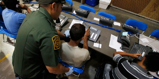 A U.S. Customs and Border Protection officer helps out a few boys who are trying to make phone calls as they are joined by hundreds of mostly Central American immigrant children that are being processed and held at the U.S. Customs and Border Protection Nogales Placement Center on Wednesday, June 18, 2014, in Nogales, Ariz. CPB provided media tours Wednesday of two locations in Brownsville, Texas, and Nogales, that have been central to processing the more than 47,000 unaccompanied children who have entered the country illegally since Oct. 1. (AP Photo/Ross D. Franklin, Pool)