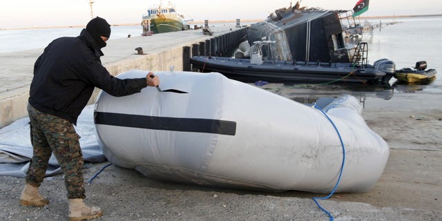 A member of the Libyan coast guard uses a knife to tear a dinghy used by migrants trying to escape to Europe last year.