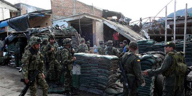 Police officers and soldiers stand in front of the destroyed police station of Inza, in Colombia's southern Cauca state, Saturday, Dec. 7, 2013. The Colombian Army said that five members of the military, two civilians and a police officer were killed after rebels of the Revolutionary Armed Forces of Colombia, FARC, threw artisanal mortar at the post from a truck, destroying that and several other buildings. (AP Photo/Juan Bautista Diaz)