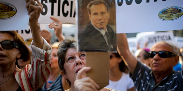 A woman chants the Argentine national anthem holding a portrait of the late prosecutor Alberto Nisman outside the AMIA Jewish community center in Buenos Aires, Argentina, Wednesday, Jan. 21, 2015. Nisman, who had been investigating the 1994 bombing of the Jewish community center that killed 85 people and who accused President Cristina Fernandez of shielding Iranian suspects, was found dead from a gunshot to the head, in his apartment late Sunday, hours before he was to testify in a Congressional hearing about the case. (AP Photo/Rodrigo Abd)