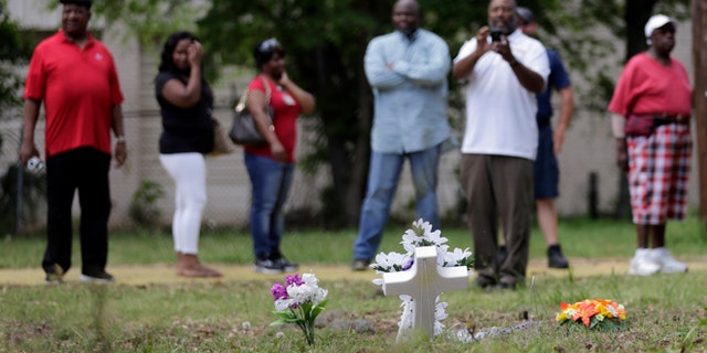 A man takes a photo as others look at a memorial and flowers placed near the site where Walter Scott was killed in North Charleston, S.C., Wednesday, April 8, 2015. Scott was killed by a North Charleston police officer after a traffic stop on Saturday. The officer has been charged with murder. (AP Photo/Chuck Burton)