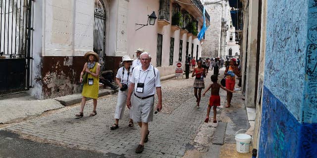 FILE - In this May 24, 2015 file photo, US tourists walks outside the Bodeguita del Medio Bar frequented by the late American novelist Ernest Hemingway in Old Havana, Cuba. Cuba's official news media announced on Thursday, July 7, 2016 the number of American travelers to the island is up 83.9 percent for the first half of the year, compared with the same January-June period in 2015. Prensa Latina reported that there were also significant increases in visitors from nations such as Spain, Italy, Poland and Germany. (AP Photo/Desmond Boylan File)