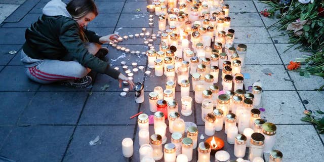 FILE- In this file photo dated Sunday, April 9, 2017, a girl lights candles in response after a highjacked truck was driven into a crowd of pedestrians and crashed into a department store in Stockholm, Sweden. A woman in her 60s who was injured in the April 7 truck attack in Stockholm has died, Swedish authorities said Friday April 28, 2017, raising the death toll to five.(AP Photo/Markus Schreiber, FILE)