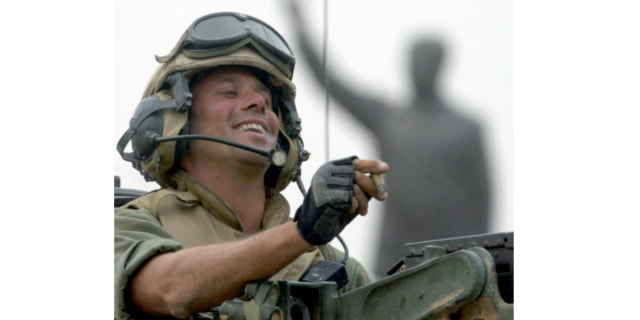 FILE: April 9, 2003: Staff Sgt. Nick Popaditch of the 3rd Battalion, 4th Marines Regiment, smokes a cigar while standing on top of his tank, as he arrives at a main crossroad in downtown Baghdad. A statue of then Iraqi President Saddam Hussein is in the background.