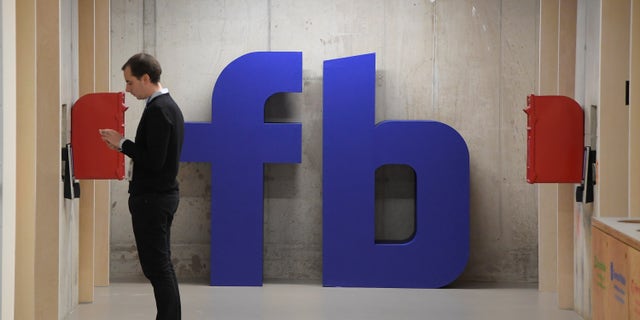 A man waits for an elevator in front of a logo at Facebook's headquarters in London, Dec. 4, 2017.