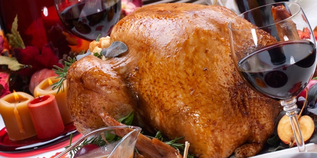 Garnished roasted turkey on holiday decorated table with pumpkins and glasses of red wine