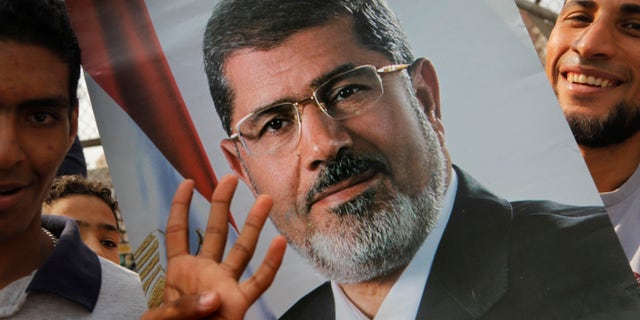 Supporters of Egypt's ousted President Mohammed Morsi raise his poster and a hand with four raised fingers, which has become a symbol of the Rabaah al-Adawiya mosque, where Morsi supporters had held a sit-in for weeks that was violently dispersed in August, during a protest in Cairo, Egypt, Friday, Nov. 8, 2013. (AP Photo/Amr Nabil)