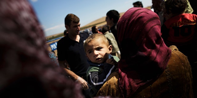 SANLIURFA, TURKEY - SEPTEMBER 30: A woman holds a boy as refugees cross the border from Syria into Turkey September 30, 2014 near Suruc, Turkey. (Photo by Carsten Koall/Getty Images)