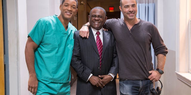 This image released by Columbia Pictures shows, from left, Will Smith, Dr. Bennet Omalu and director Peter Landesman on the set of the film, "Concussion." Smith plays Omalu, a Nigerian-born forensic pathologist in Pittsburgh who knows nothing about football when he performs the autopsy on former Steelers center Mike Webster. Omalu discovers CTE in Webster's brain, setting him on a journey that exposes the concussion crisis. (Melinda Sue Gordon/Columbia Pictures via AP)