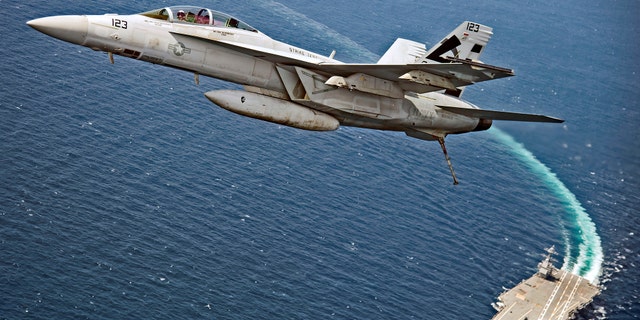 An F/A-18F Super Hornet jet flies over the USS Gerald R. Ford.