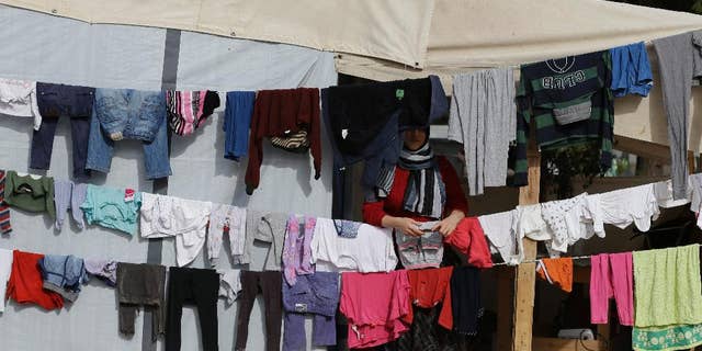 A woman stands behind her laundry at the refugee camp of Ritsona about 86 kilometers (53 miles) north of Athens, on Tuesday, Nov. 22, 2016. Around 680 people are staying in new container houses as over 62,000 refugees and migrants are stranded in Greece after a series of Balkan border closures. (AP Photo/Thanassis Stavrakis)