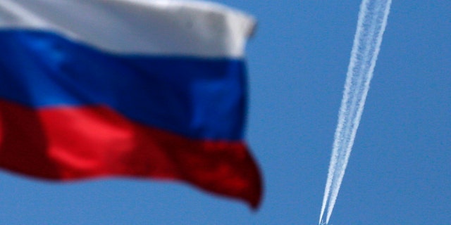 File photo - A contrail left by a passenger plane is seen behind a Russian state flag as it passes over the Siberian city of Krasnoyarsk, August 7, 2014. (REUTERS/Ilya Naymushin)
