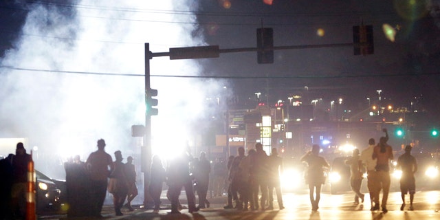 Aug. 18, 2014: People stand near a cloud of tear gas in Ferguson, Mo. during protests for the Aug. 9 shooting of unarmed black 18-year-old Michael Brown by a white police officer