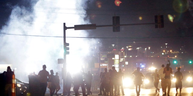 Aug. 18, 2014: People stand near a cloud of tear gas in Ferguson, Mo. during protests for the Aug. 9 shooting of unarmed black 18-year-old Michael Brown by a white police officer