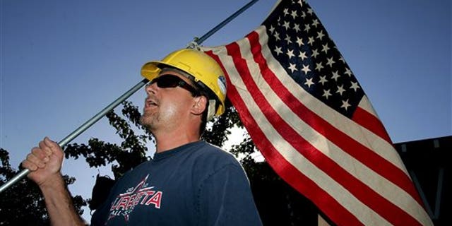 Paul Hathaway, of Murrieta, Calif., holds a U.S. flag as he shouts outside Murrieta Mesa High School in Murrieta, Calif., where city, Riverside County and federal officials spoke about a plan to process immigrants detained in Texas at the Murrieta U.S. Border Patrol facility, Wednesday, July 2, 2014. (AP Photo/The Press-Enterprise, Terry Pierson)
