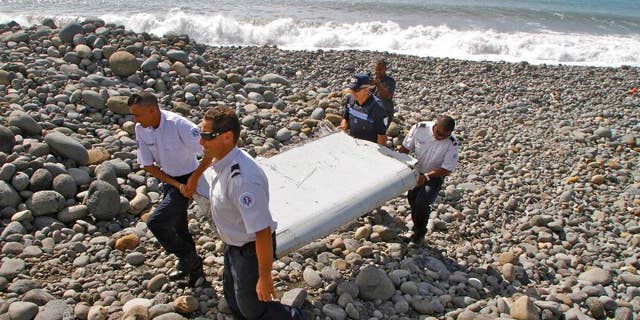 FILE - In this July 29, 2015, file photo, French police officers carry a piece of debris from a plane known as a flaperon in Saint-Andre, Reunion Island. The barnacle-encrusted part was the first trace of Malaysia Airlines Flight 370 that disappeared two years ago. Malaysia's confirmation on Thursday, May 12, 2016, that other debris found in March 2016 came from missing Malaysia Airlines Flight 370 brings to five the number of parts that have been recovered from the aircraft that vanished two years ago. (AP Photo/Lucas Marie, File)