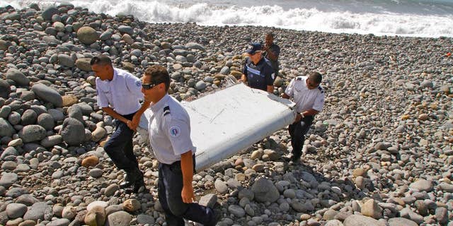 FILE - In this July 29, 2015, file photo, French police officers carry a piece of debris from a plane known as a flaperon in Saint-Andre, Reunion Island. The barnacle-encrusted part was the first trace of Malaysia Airlines Flight 370 that disappeared two years ago. Malaysia's confirmation on Thursday, May 12, 2016, that other debris found in March 2016 came from missing Malaysia Airlines Flight 370 brings to five the number of parts that have been recovered from the aircraft that vanished two years ago. (AP Photo/Lucas Marie, File)