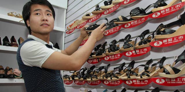 FILE--In this a Tuesday, June 23, 2015 file photo, ofChinese national Wei Kun as he adjusts a display as he waits for customers at his shoe shop in Kampala, Uganda. Years of growing animosity at Chinese traders turned into a protest by hundreds in Uganda's capital on Wednesday April 19, 2017 against what local businesses called unfair competition, while the mayor warned against the tensions turning into xenophobic attacks. (AP Photo/Stephen Wandera-File)