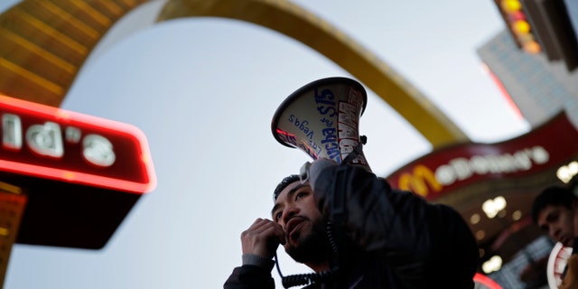 A protestor speaks on a bullhorn as he and others protest near a McDonald's restaurant along the Las Vegas Strip, Tuesday, Nov. 29, 2016, in Las Vegas. The protest was part of the National Day of Action to Fight for $15. The campaign seeks higher hourly wages, including for workers at fast-food restaurants and airports.