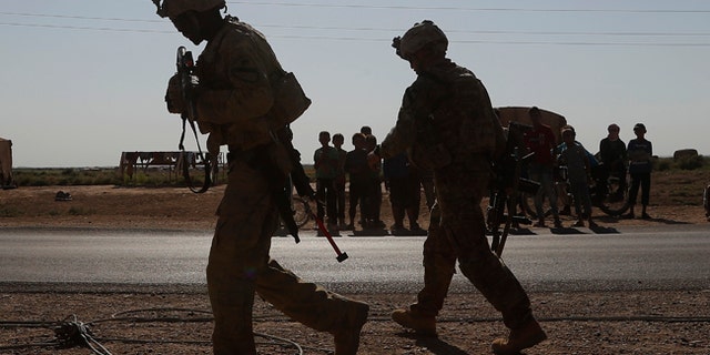 U.S. soldier, foreground, walk in front of Syrian children in the background, at a road that links to Raqqa, northeat Syria, July 26, 2017.