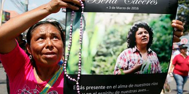 FILE - In this March 16, 2016, file photo, a woman holds up a poster with a photo of slain environmental leader Berta Caceres, during a protest march in Tegucigalpa, Honduras. Authorities said that unidentified gunmen killed Nelson Garcia, a colleague of Caceres, who was slain almost two weeks ago in similar circumstances. Honduran authorities announced Thursday, Sept. 8, that they have arrested a sixth suspect in the March killing of environmental activist Berta Caceres. (AP Photo/Fernando Antonio, File)