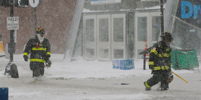 Boston firefighters wading through a street flooded from tidal surge.