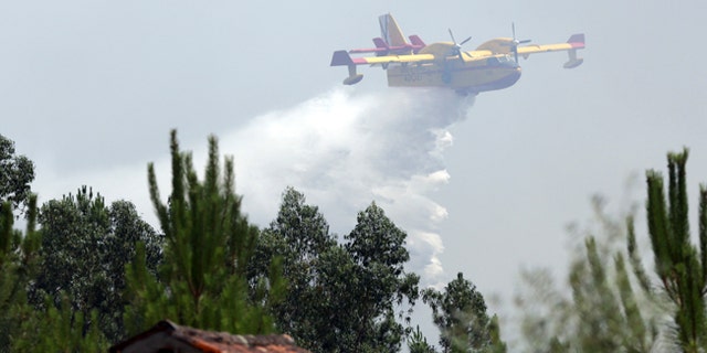 A firefighting airplane drops its load of water trying to prevent a forest fire from reaching the village of Ouzenda, outside Pedrogao Grande, central Portugal, Tuesday, June 20 2017. Ouzenda residents were evacuated and firefighters moved in to protect the houses while aircraft battled the fire approaching the small village. Emergency services in Portugal said Tuesday they were making headway in their battle to control a major wildfire that killed more than 60 people in the central region of the country. (AP Photo/Armando Franca),