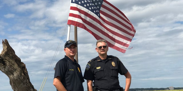 Officers Captain Ashley Brown, left, and Lt. Greg Ernst stand next to the American flag they rescued on Patriots Day.