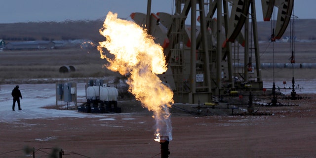 Oct. 22, 2015: Workers tend to oil pump jacks behind a natural gas flare near Watford City, N.D.