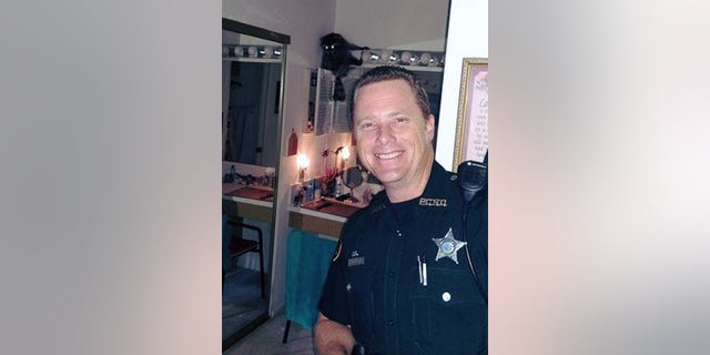 A sheriff's deputy poses with the raccoon frozen in fear in the bathroom.