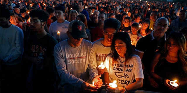 Jorge Zapata, Jr., center, a student at Marjory Stoneman Douglas High School, holds candles with his mother Lavinia Zapata, and father Jorge Zapata, Sr., during a candlelight vigil Wednesday.