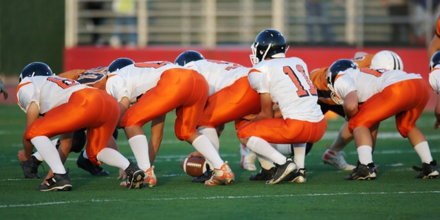 High school football players in their play stance at the line of scrimmage during a football game