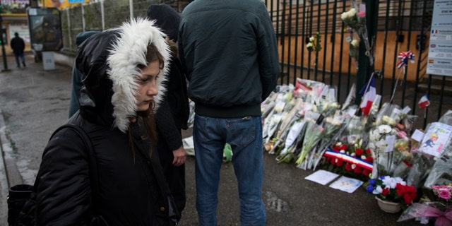 People stand next to flowers placed at the main gate of the police headquarters in Carcassonne, France, on March 24, 2018.