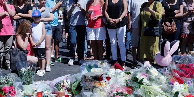 People stand by flowers laid near the scene where a truck mowed through revelers in Nice, southern France, Friday, July 15, 2016. A large truck mowed through revelers gathered for Bastille Day fireworks in Nice, killing more than 80 people and sending people fleeing into the sea as it bore down for more than a mile along the Riviera city's famed waterfront promenade. (AP Photo/Francois Mori)