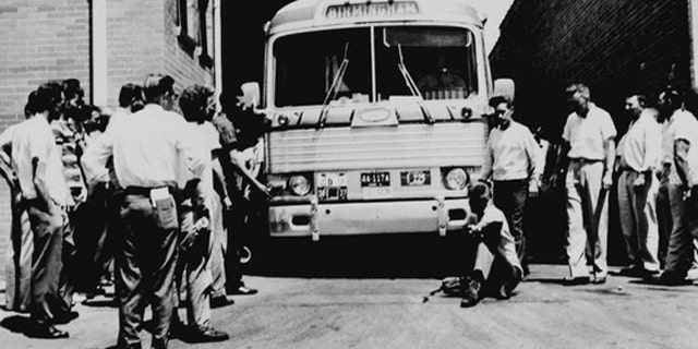 May 14, 1961: An unidentified white man sits in front of a Greyhound bus to prevent it from leaving the station with a load of Freedom Riders testing bus station segregation in Anniston, Ala., as other white men mill around station. The bus was stopped by a flat tire and surrounded by a white crowd outside Anniston, and burned a short time later. The passengers got out without serious injury. (AP)