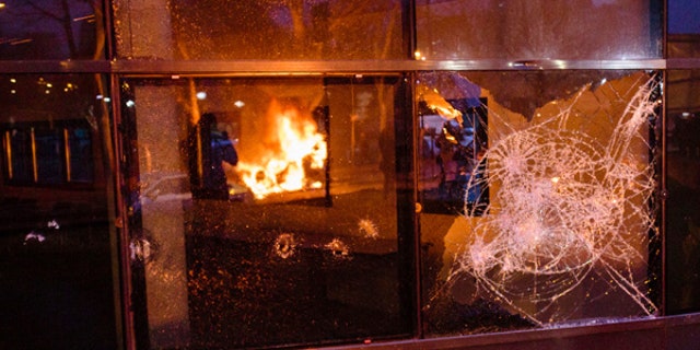 A fire set up by protestors is reflected in a broken window after a demonstration in Bobigny outside Paris, Saturday, Feb. 11, 2017. A peaceful demonstration protesting the alleged rape of a black youth by police has degenerated, with small groups setting at least one vehicle afire and throwing projectiles at police. (AP Photo/Aurelien Morissard)