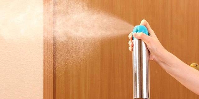 Sprayed air freshener in hand on room background